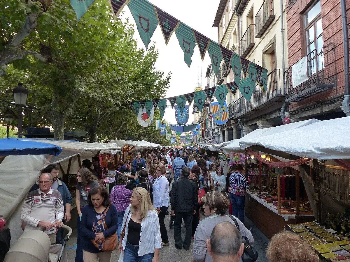 Mercado Cervantino de Alcal&aacute; de Henares con visitantes recorriendo los puestos, evento tur&iacute;stico clave para estrategias de redes sociales de negocios locales